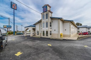 A motel with a prominent '6' sign, a covered parking area, and a clear sky.