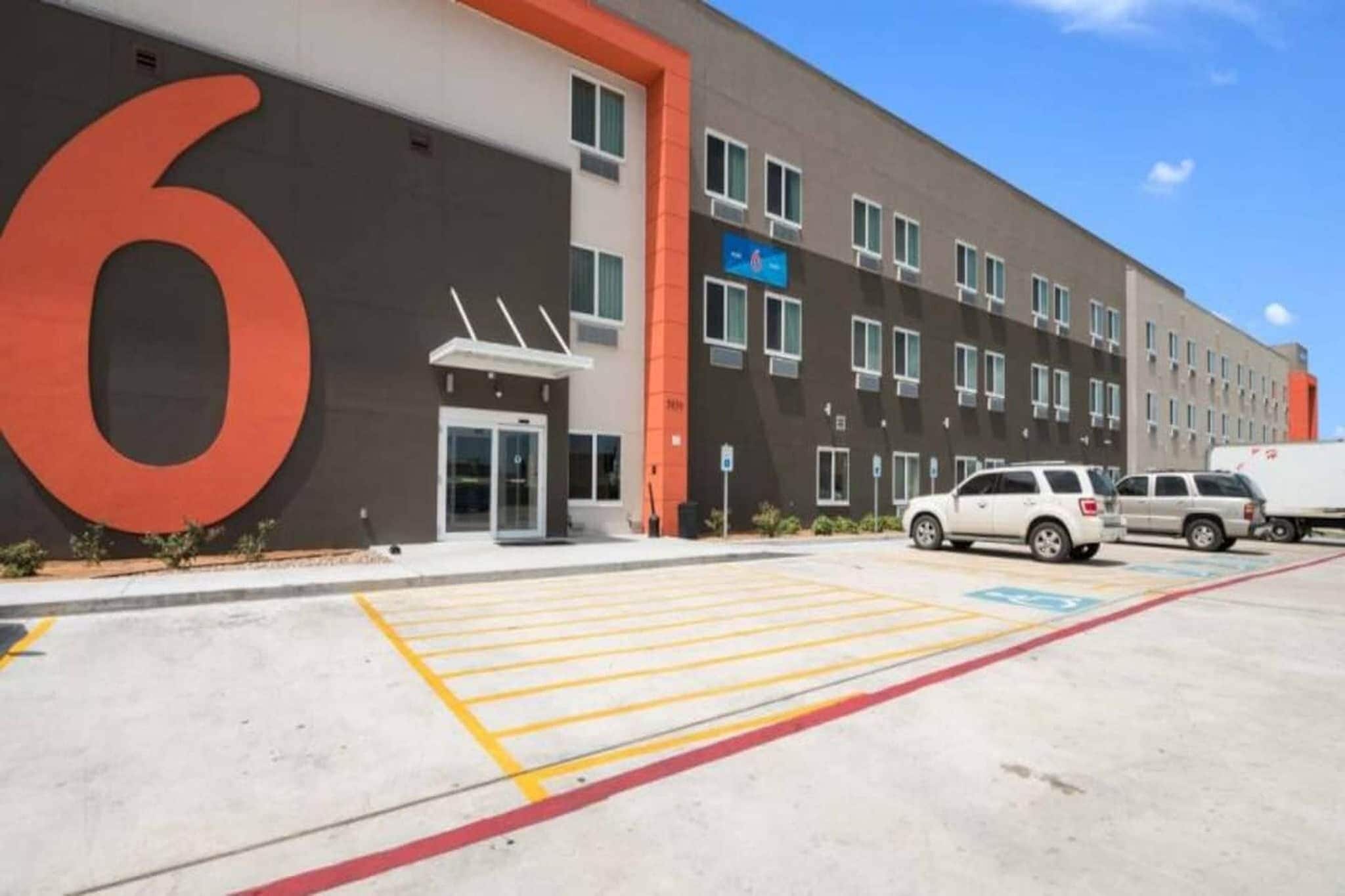 Un edificio moderno con un gran letrero con el número '6', un estacionamiento con espacios delimitados y un cielo despejado.