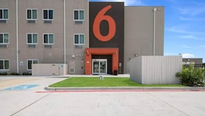 Un bâtiment moderne, reconnaissable à son grand panneau indiquant le chiffre « 6 », doté d’une entrée sécurisée et d’un espace de stationnement avec un emplacement réservé aux personnes handicapées.