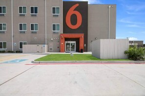 Um edifício moderno com um grande letreiro '6', entrada com portão e área de estacionamento com vaga para deficientes.