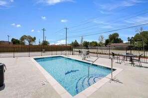 Una piscina rectangular con una escalera de metal, rodeada por una solana de concreto y una cerca de metal.