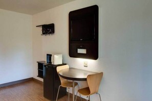 A small, modern room with a round dining table, two chairs, a black cabinet, and a mounted TV.