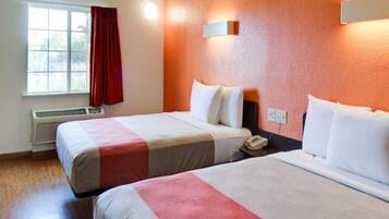 A hotel room with two beds, a window with red curtains, an air conditioning unit, and a wall-mounted telephone.