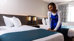 Una habitación de hotel con dos camas, una mesita de noche con lámpara y un ventanal con cortinas estampadas.