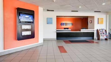 A hotel reception area with a digital screen, a reception desk, and a magazine rack.