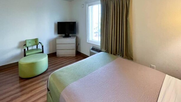 A hotel room with a bed, a chair, a television, and a window with curtains. - 1 Queen Bed|Mobil Access|Nsmk|Kitchen (Belmont)