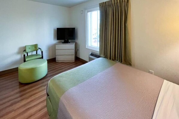 Een hotelkamer met een bed, een stoel, een televisie en een raam met gordijnen.