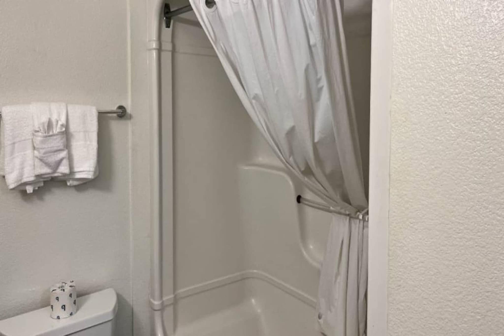 A bathroom with a shower curtain, a towel rack with folded towels, and a toilet.