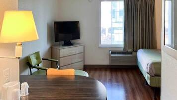 Una habitación de hotel con una mesa de comedor, un televisor, un sofá y un ventanal con cortinas.