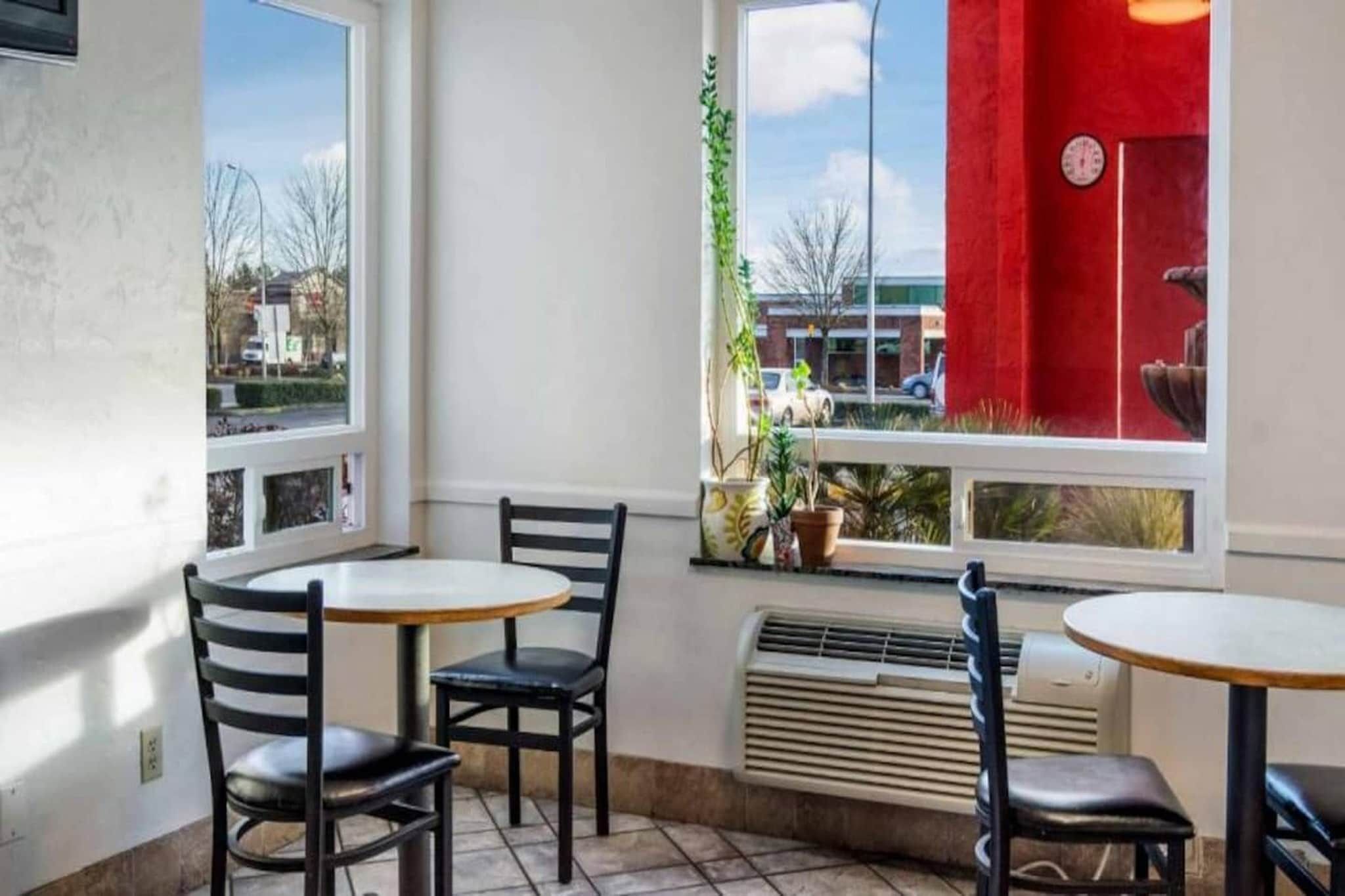 A corner room with two tables and chairs, a window with a view of the street, and a red wall.