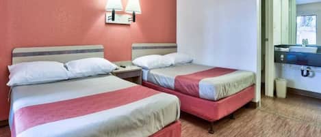 A hotel room with two beds, a nightstand, a wall-mounted lamp, and a bathroom with a sink and mirror.