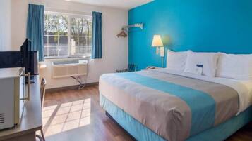 Una habitación de hotel con cama, escritorio, silla, lámpara y ventana con cortinas.