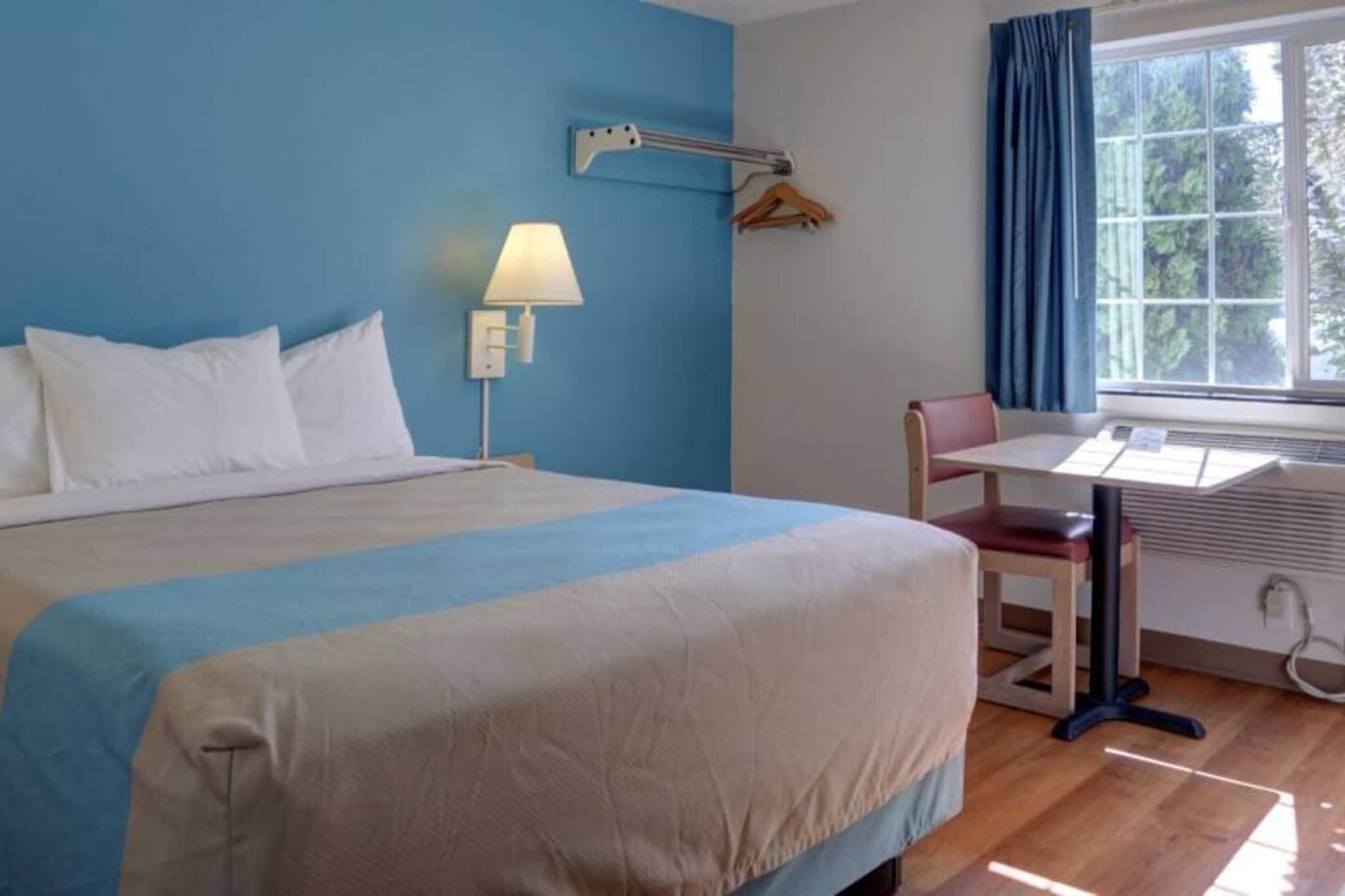 A hotel room with a bed, a desk, a chair, a lamp, and a window with curtains.
