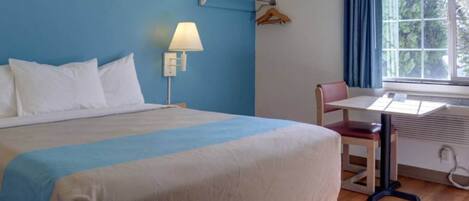 Una camera d'albergo con un letto, una scrivania, una sedia, una lampada e una finestra con tende.