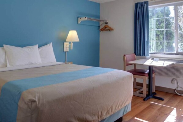 A hotel room with a bed, a desk, a chair, a lamp, and a window with curtains.