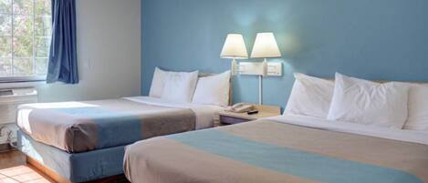 Une chambre d’hôtel avec deux lits, une fenêtre avec des rideaux, un appareil de climatisation et une table de chevet avec une lampe.