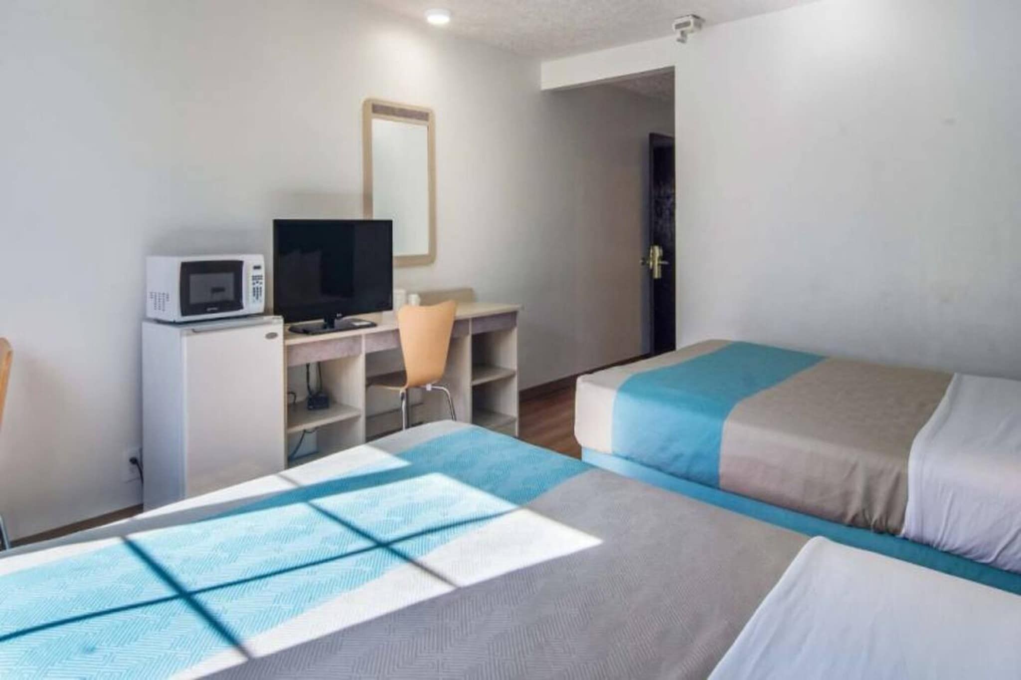 A hotel room with two beds, a desk with a computer and a TV, and a microwave.