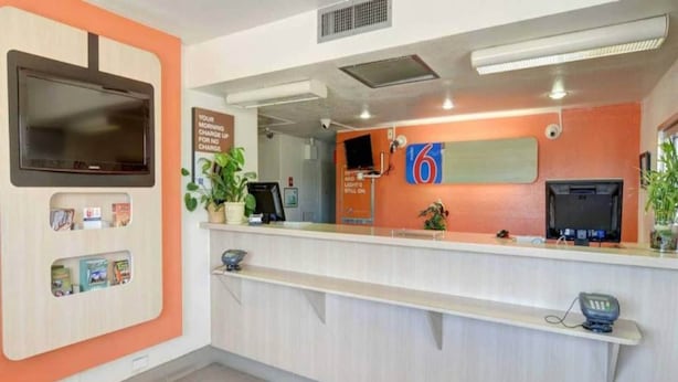 Un mostrador de recepción con un televisor de pantalla plana, un reloj digital y una planta.