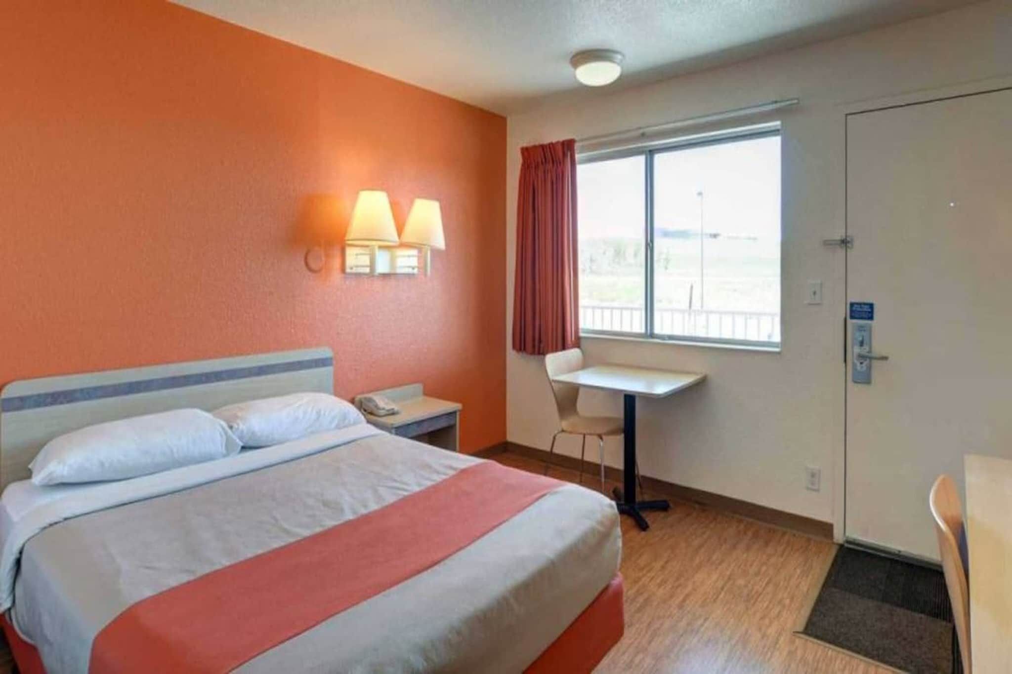 Een hotelkamer met een bed, nachtkastje, lamp, stoel, bureau, raam en deur.