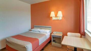 Habitación de hotel con cama, mesita de noche, lámpara y un pequeño escritorio con una silla.