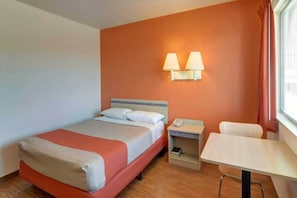 Une chambre d’hôtel comprenant un lit, une table de chevet, une lampe et un petit bureau avec une chaise.