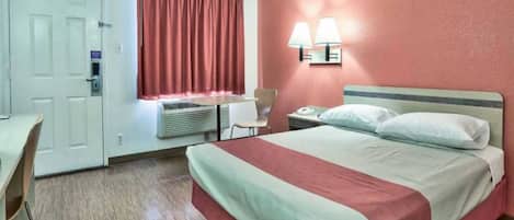 A hotel room with a bed, a desk, a chair, an air conditioning unit, and a window with curtains.
