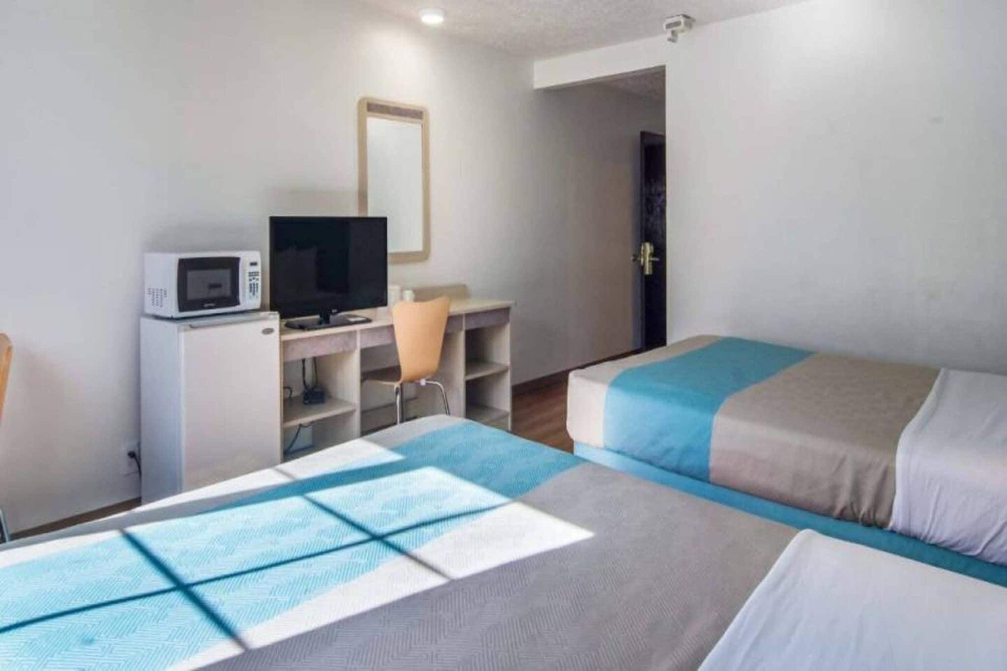 Ein Hotelzimmer mit zwei Betten, einem Schreibtisch mit Computer und Fernseher sowie einer Mikrowelle.