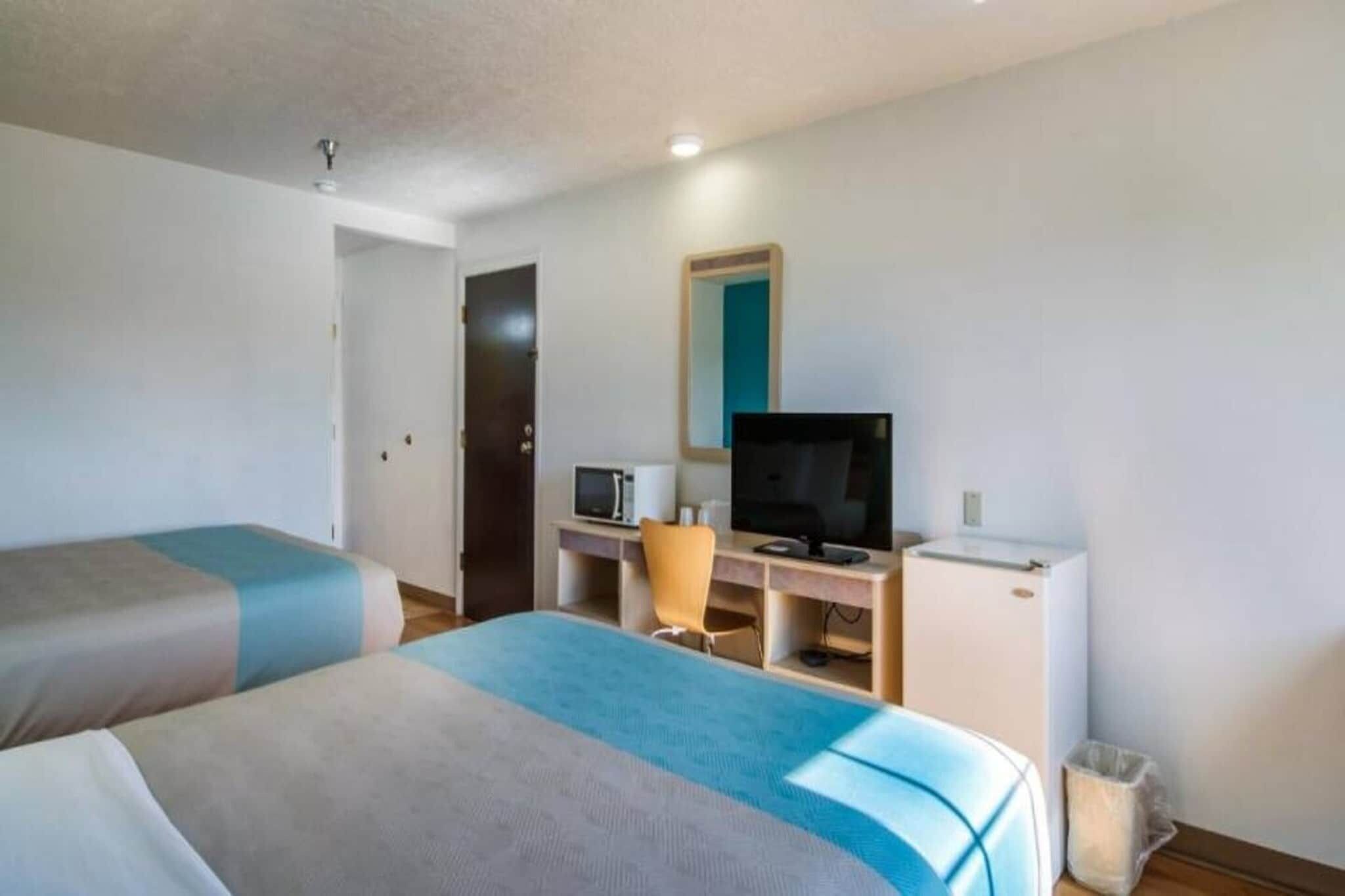 A hotel room with two beds, a desk with a television, a chair, and a small refrigerator.