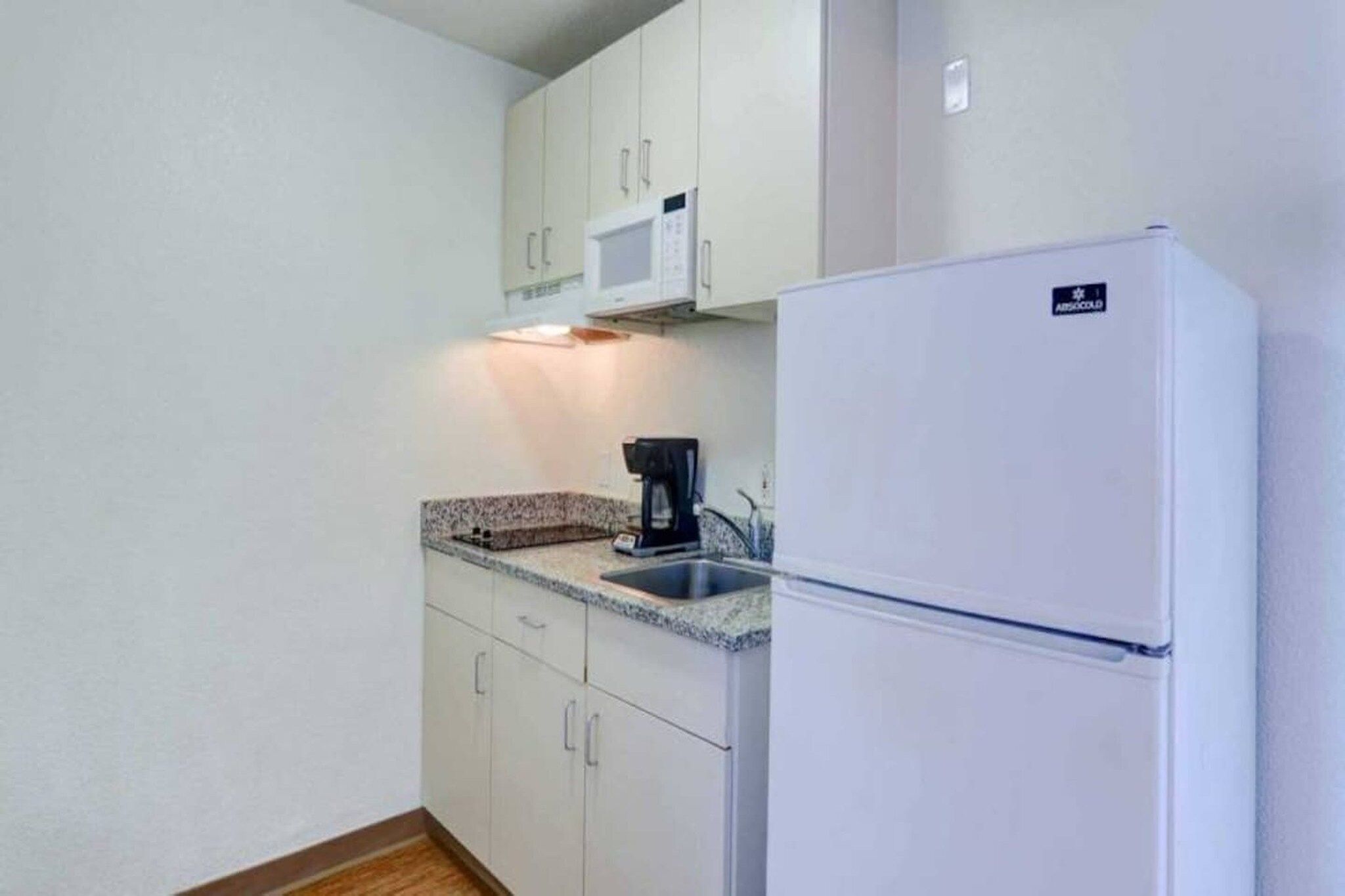 Una cocina compacta con gabinetes blancos, microondas, cafetera y refrigerador.