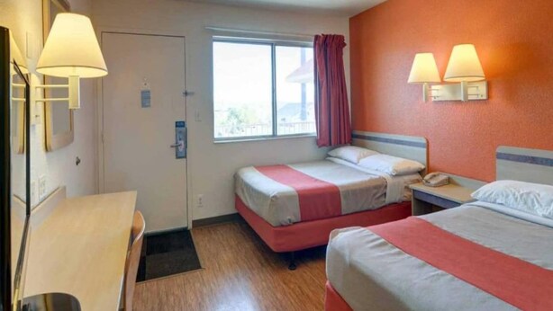 Quarto de hotel com duas camas, uma escrivaninha, janela com cortinas e luminárias fixadas na parede.