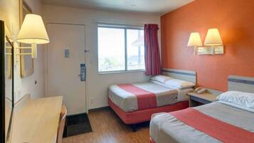 Habitación de hotel con dos camas, un escritorio, una ventana con cortinas y lámparas fijadas a la pared.