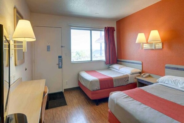 Een hotelkamer met twee bedden, een bureau, een raam met gordijnen en wandlampen.