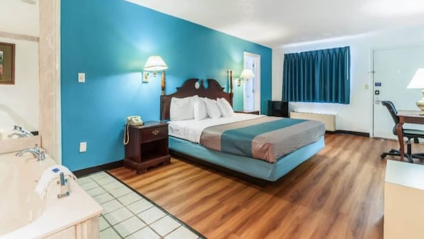 Quarto de hotel com cama, mesas de cabeceira, escrivaninha e uma cadeira.