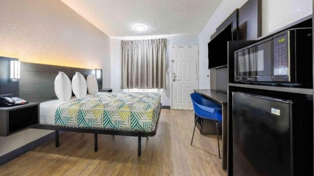 A hotel room with a bed, a desk, a chair, a refrigerator, and a door. - 1 King Bed|Smoking|Fort Worth (Fort Worth TX)