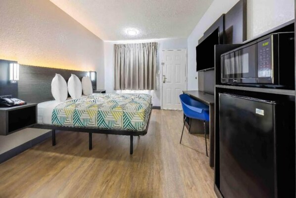 Une chambre d’hôtel avec un lit, un bureau, une chaise, un réfrigérateur et une porte.