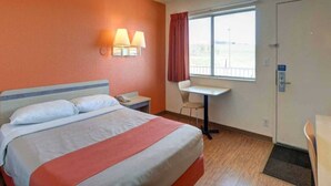 Quarto de hotel com cama, escrivaninha, cadeira, janela e porta.