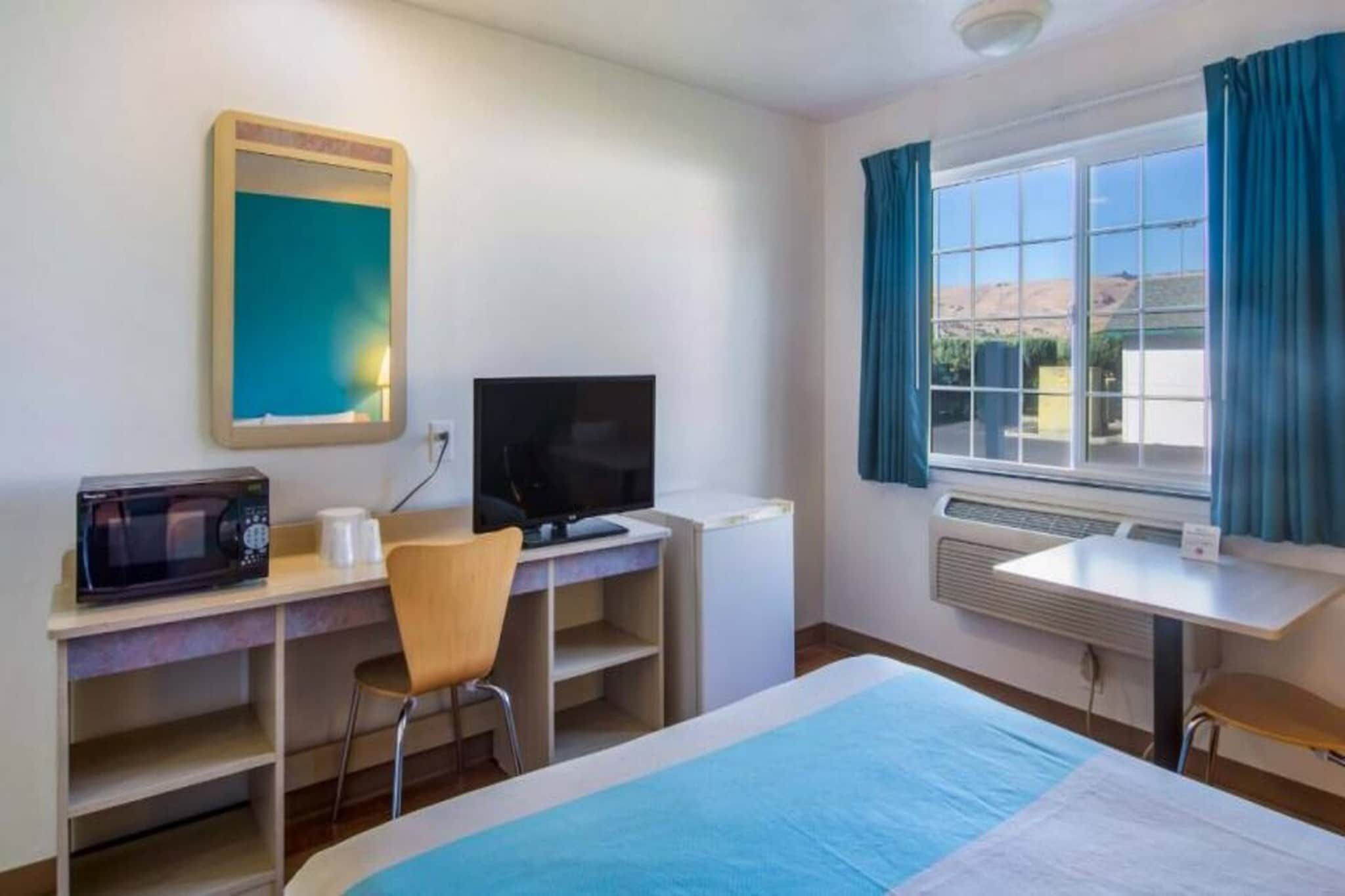 Une chambre d’hôtel avec un lit, un bureau avec un ordinateur, une chaise, un four à micro-ondes et une fenêtre avec des rideaux.