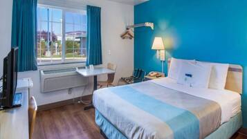 A hotel room with a bed, a desk, a chair, a window with curtains, a lamp, and a telephone.