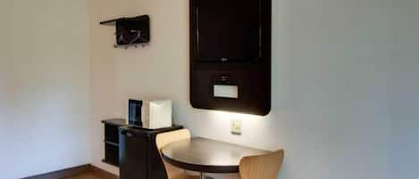 A small, modern room with a round dining table, two chairs, a black cabinet, and a mounted TV.