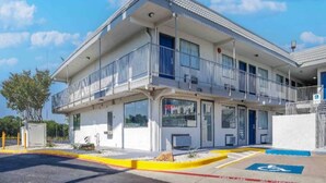A two-story motel with a balcony on the second floor, a parking lot with a handicapped parking space, and a clear blue sky. - 1 Queen Bed|Smoking|Fort Worth (Fort Worth TX)