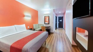 Una habitación de hotel con una cama, un escritorio, una silla, un televisor y un pasillo.