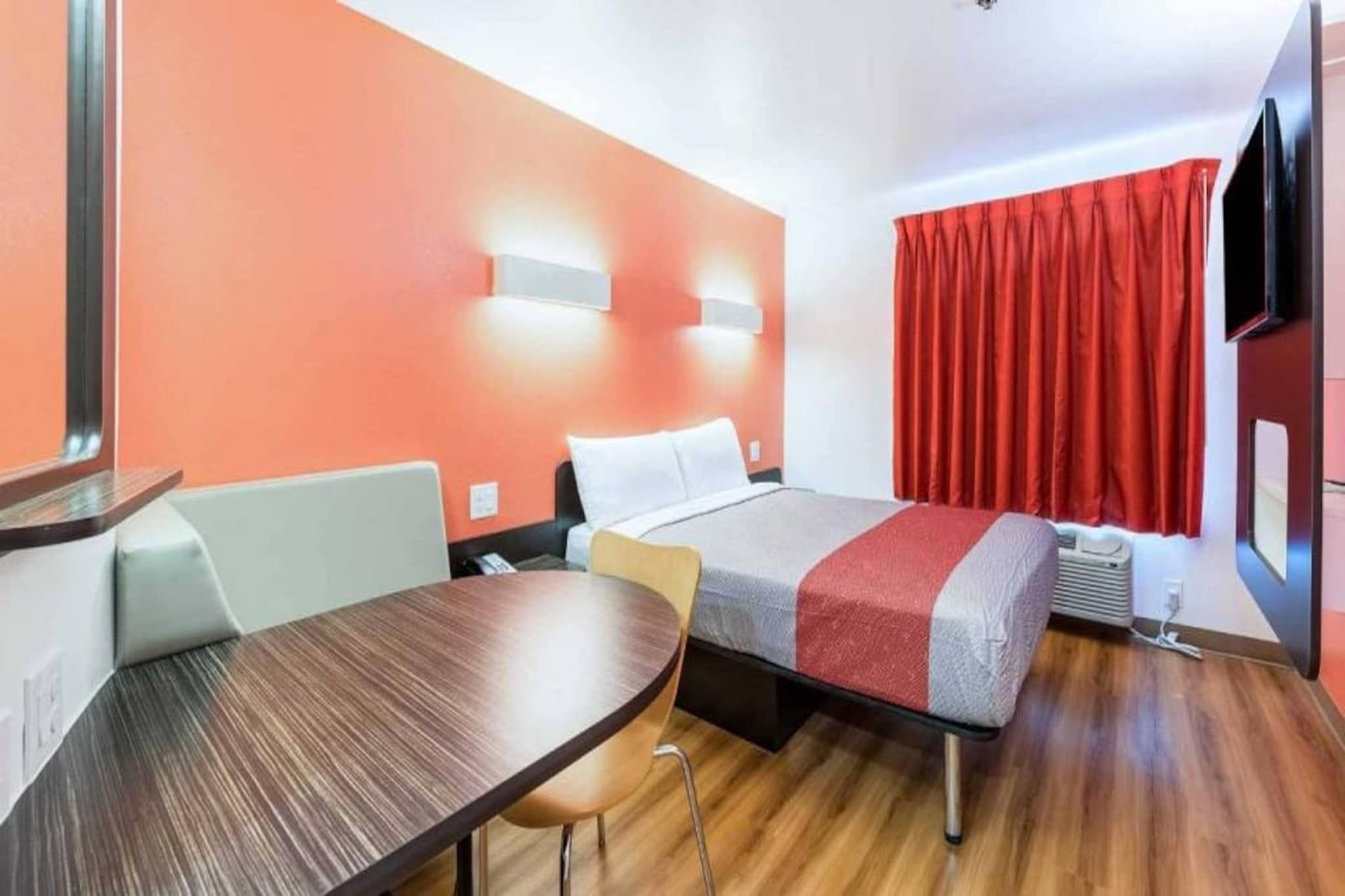 A hotel room with a bed, a desk, a chair, a TV, and a window with curtains.