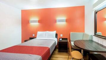 A hotel room with a bed, a desk, a chair, and a large mirror.