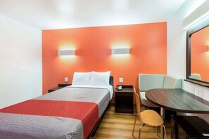 Ett hotellrum med en säng, ett skrivbord, en stol och en stor spegel.