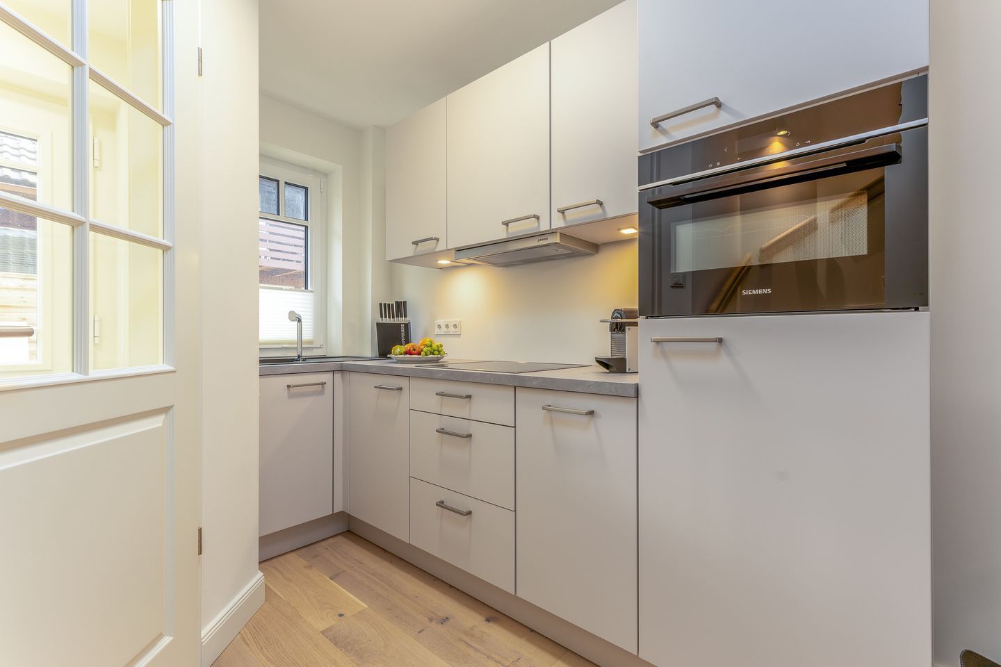 A modern kitchen with white cabinetry, a built-in oven, and a window providing natural light.