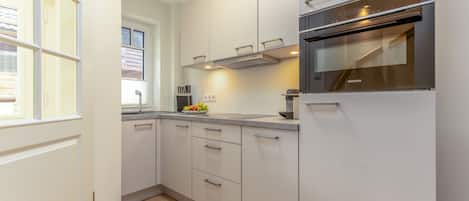 Een moderne keuken met witte kastjes, een ingebouwde oven en een raam dat voor natuurlijk licht zorgt.