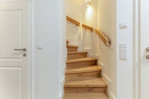 A staircase with wooden steps and a wooden handrail, leading to a landing with a light switch. - Nordseenest 2 - Exclusive vacation rental on Sylt with a terrace and modern (Sylt)