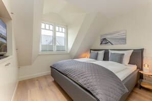 A bedroom with a bed, a window, a painting, and a bedside lamp. - Nordseenest 2 - Exclusive vacation rental on Sylt with a terrace and modern (Sylt)