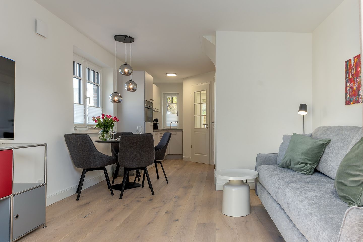 A modern living room with a grey sofa, a small white side table, and a grey couch with green cushions.