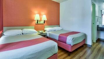 Habitación de hotel con dos camas, una mesita de noche, una lámpara y un baño visible a través de una puerta abierta.